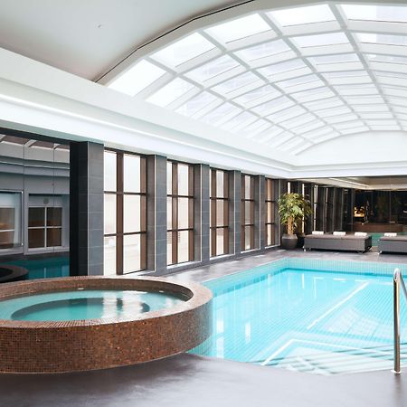 Hotel Stamford Plaza Melbourne Esterno foto The photo shows an indoor swimming pool area. The pool is rectangular and has clear blue water, surrounded by a sleek, modern design. On one side, there is a round hot tub made of dark stone. Large windows line the walls, allowing natural light to fi