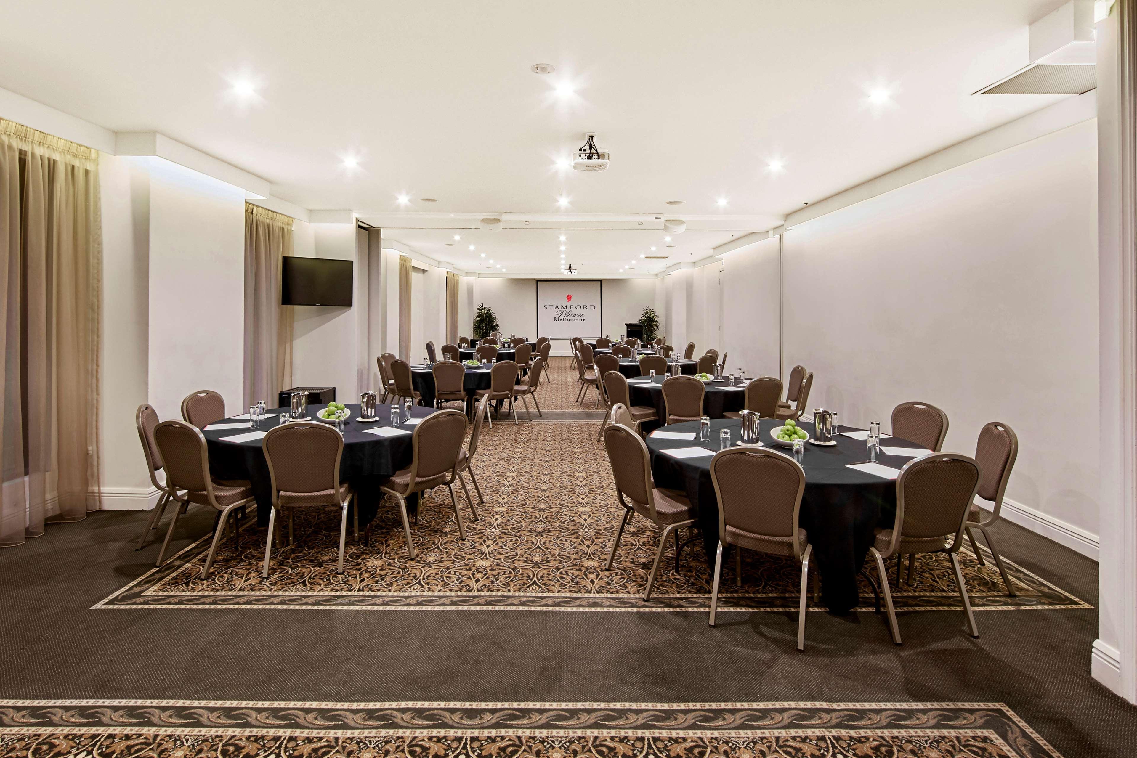 Hotel Stamford Plaza Melbourne Esterno foto The photo shows an event space or banquet hall set up for a gathering. The room features several round tables covered with black tablecloths, each adorned with small centerpieces. Chairs are arranged around each table. The lighting is bright and mode