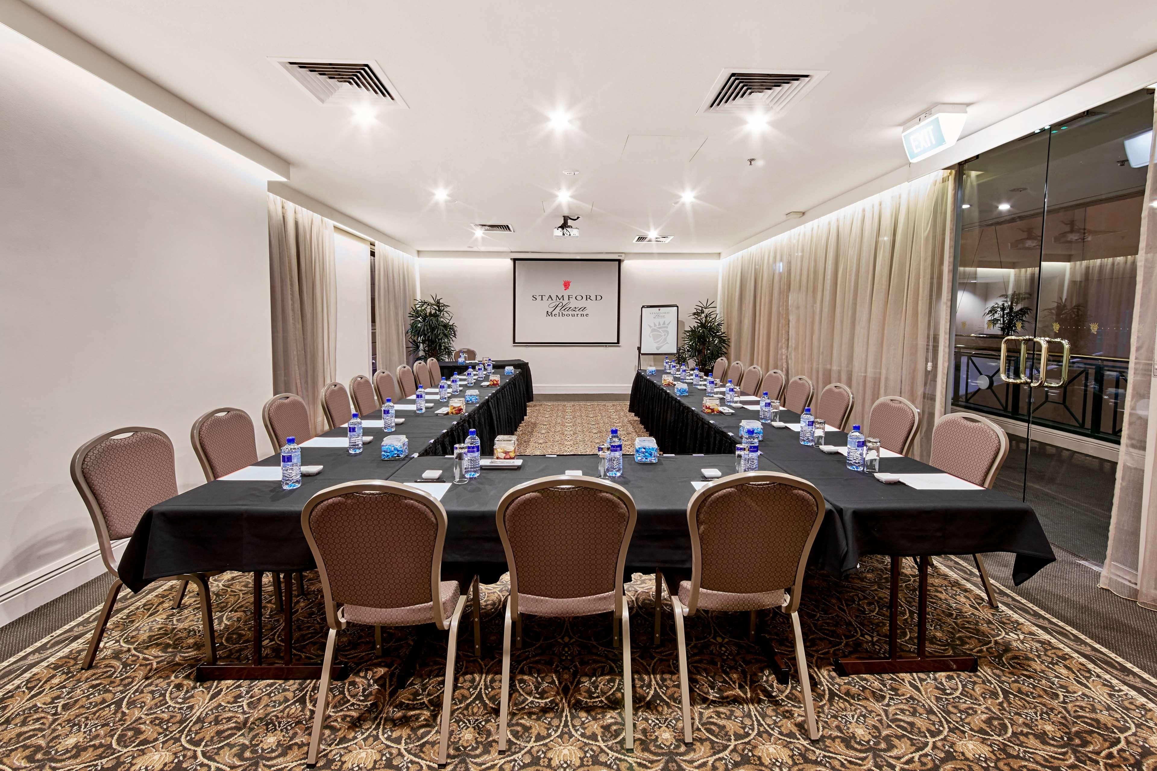 Hotel Stamford Plaza Melbourne Esterno foto The photo shows a conference room set up for a meeting. There are several long tables arranged in a U-shape, covered with black tablecloths. Each table has a water bottle and notepad placed at intervals. The room is well-lit, with light-colored walls