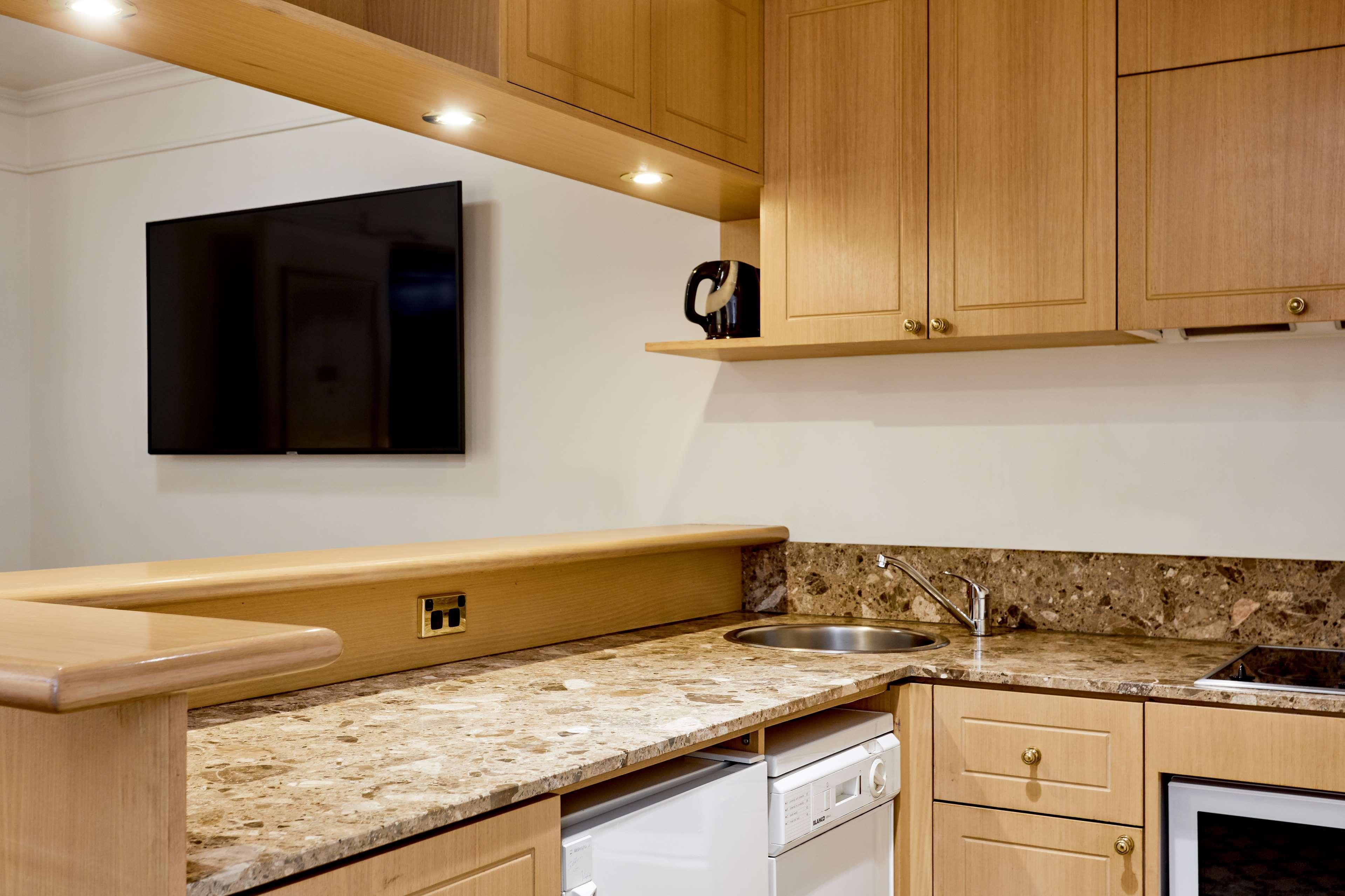 Hotel Stamford Plaza Melbourne Esterno foto The photo shows a modern kitchen with wooden cabinetry and a granite countertop. There's a stainless steel sink integrated into the countertop, and appliances including a dishwasher and possibly a coffee maker on the shelf above. A flat-screen televi
