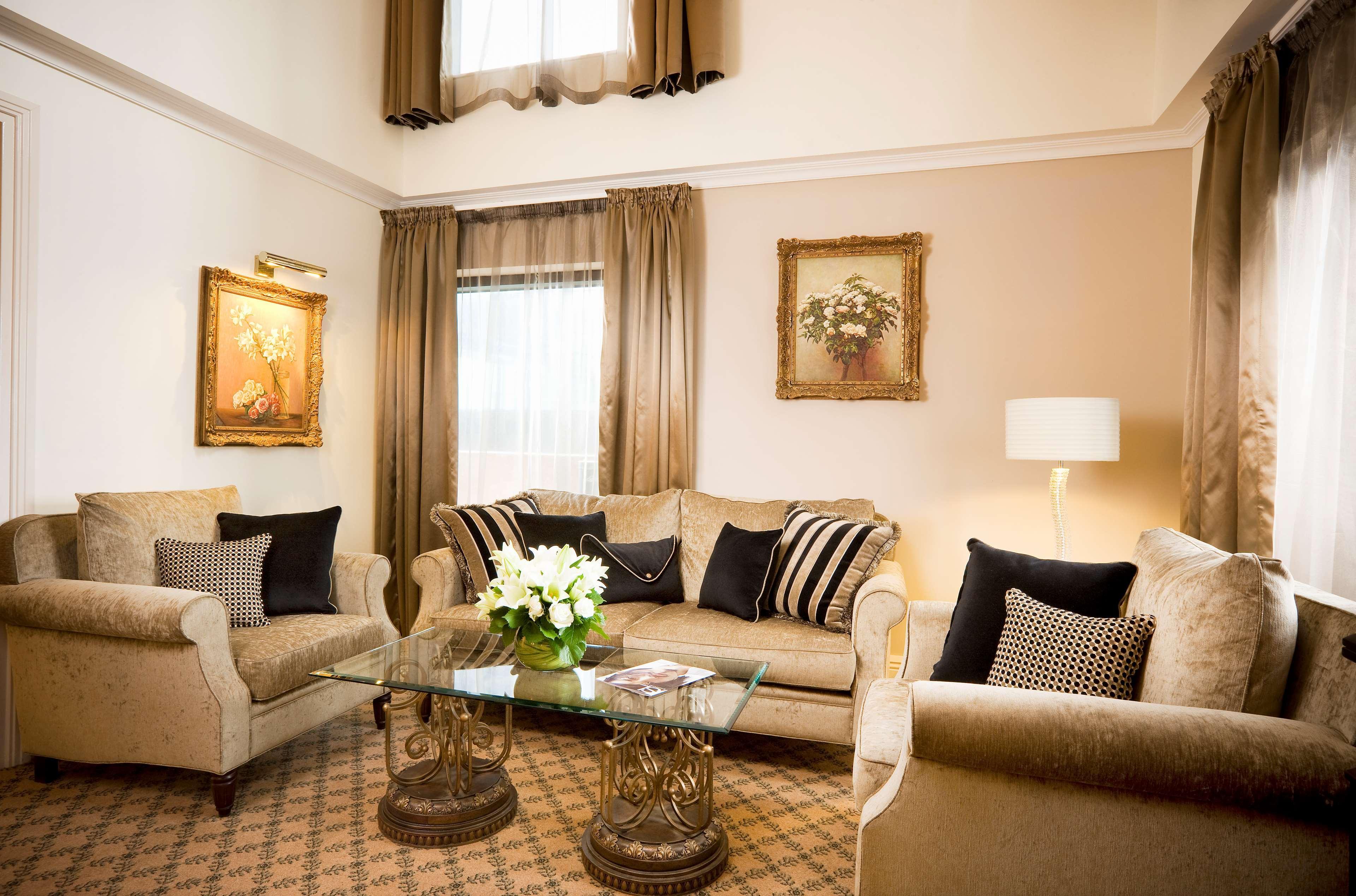 Hotel Stamford Plaza Melbourne Camera foto The photo depicts a stylish living room with a warm and inviting aesthetic. It features a set of comfortable beige sofas adorned with decorative pillows in black and patterned designs. There is a glass coffee table at the center, supported by elegant