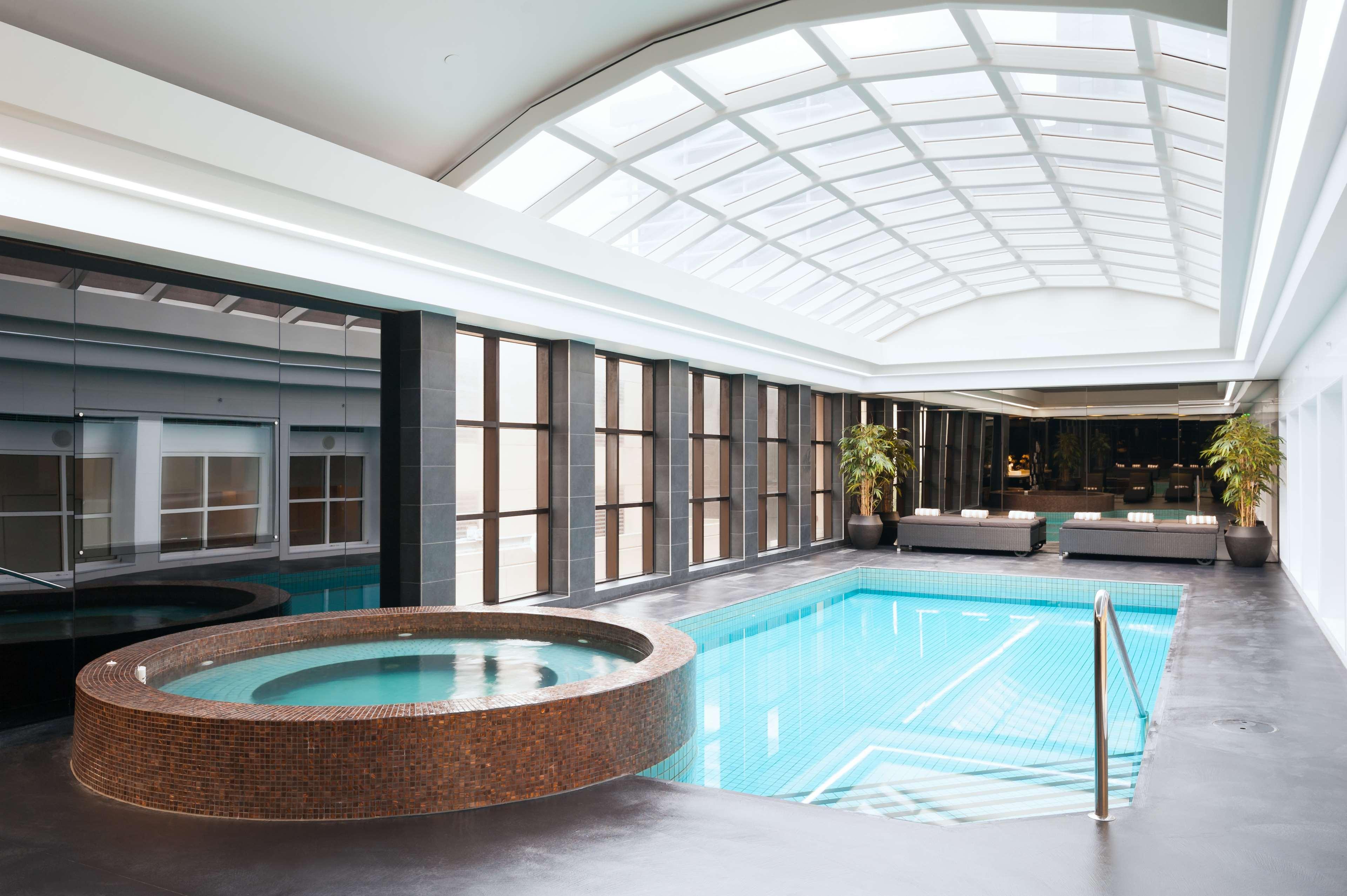 Hotel Stamford Plaza Melbourne Esterno foto The photo shows an indoor swimming pool area. The pool is rectangular and has clear blue water, surrounded by a sleek, modern design. On one side, there is a round hot tub made of dark stone. Large windows line the walls, allowing natural light to fi