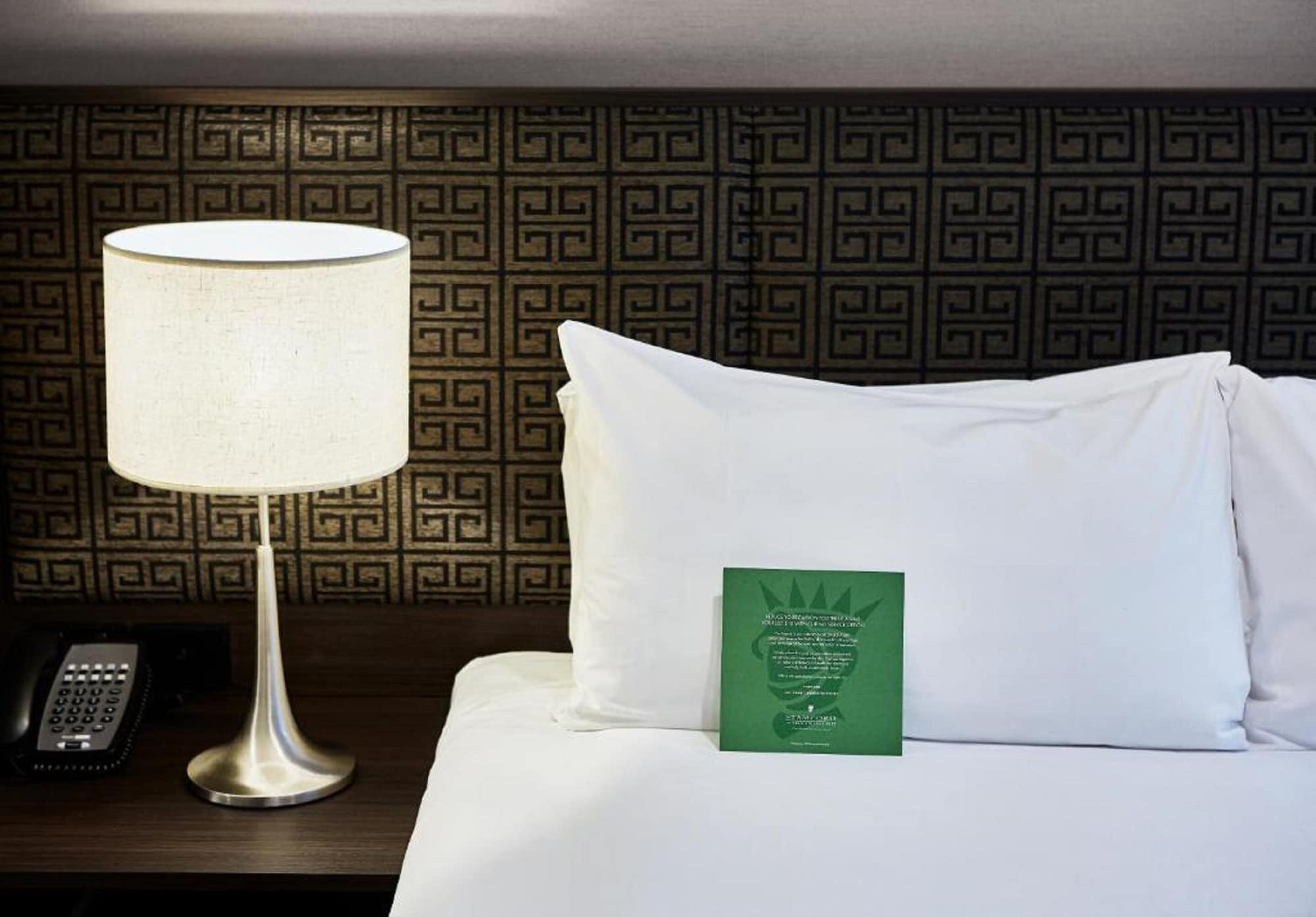 Hotel Stamford Plaza Melbourne Esterno foto The photo shows a neatly made bed with a white pillow and a green item placed on top of it. Next to the bed, there is a stylish table lamp with a lampshade that appears to be white. In the background, you can see a patterned wall, which has a geometr