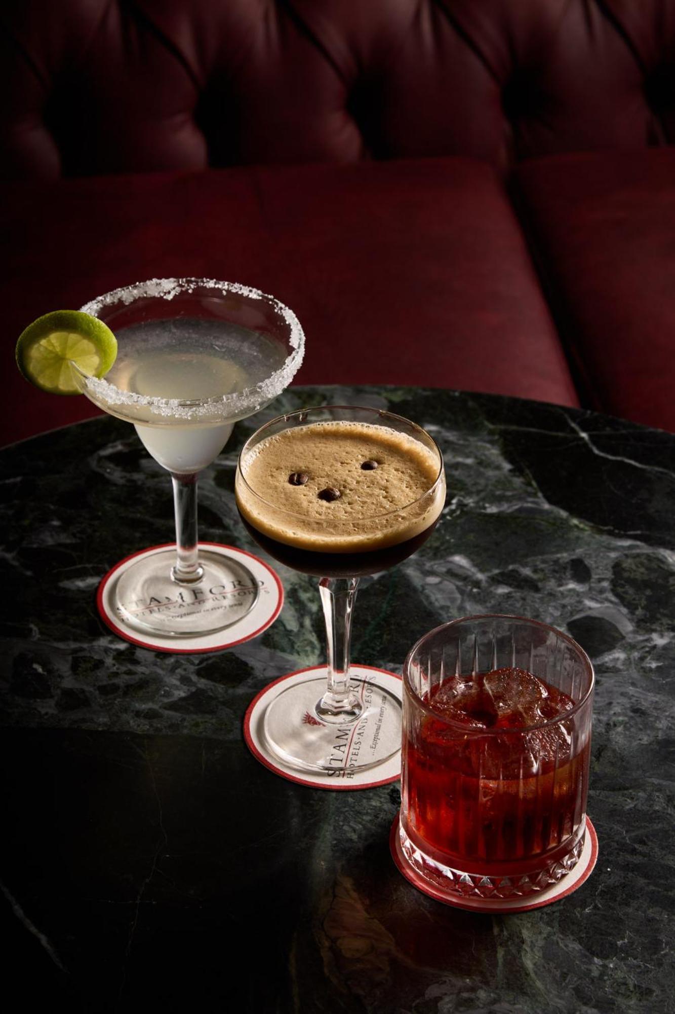 Hotel Stamford Plaza Melbourne Esterno foto The photo displays three different cocktails arranged on a dark marble table. 

1. On the left, there is a margarita glass filled with a clear drink, garnished with a lime slice and featuring a salted rim.
2. In the center, a coupe glass holds a dark