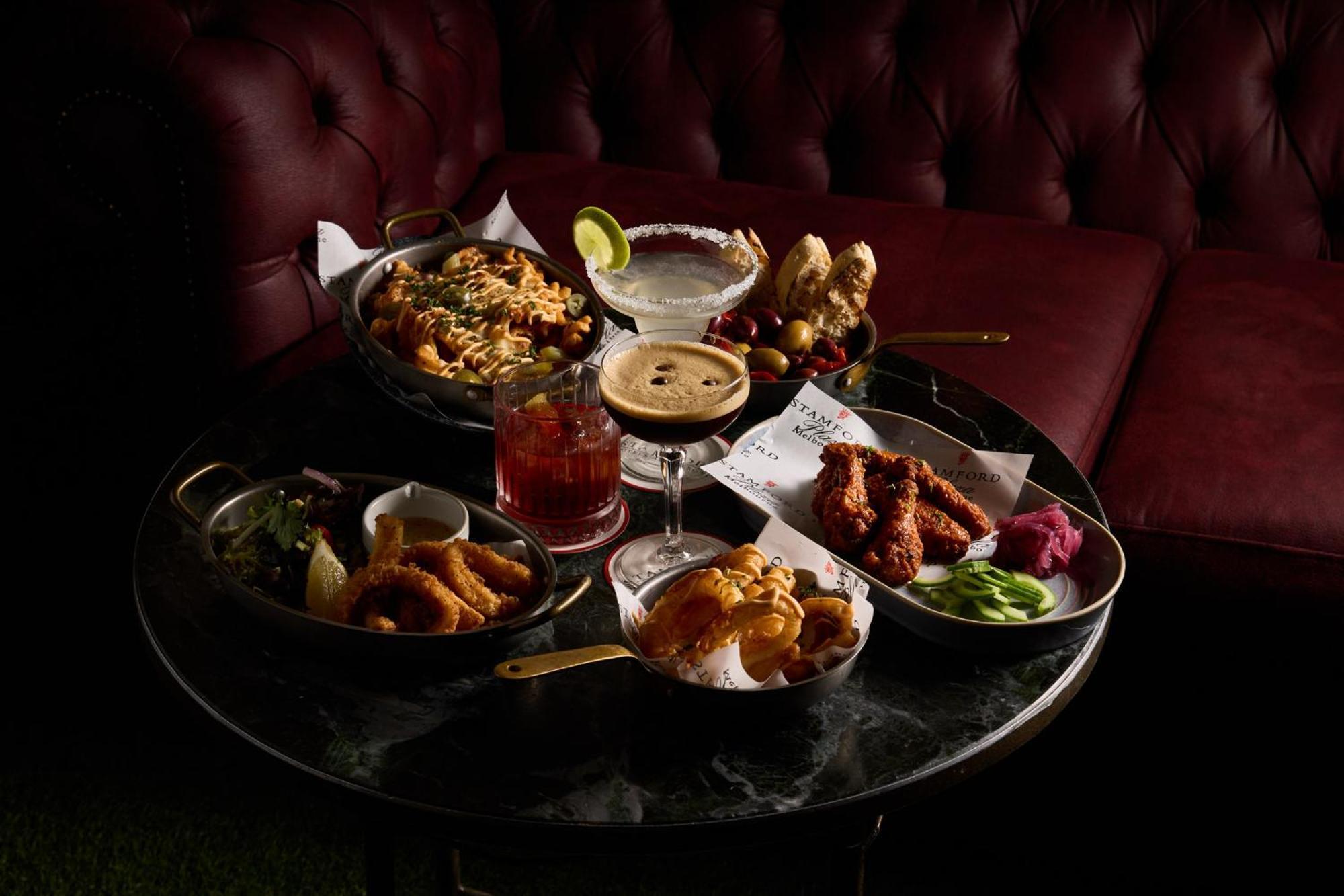 Hotel Stamford Plaza Melbourne Esterno foto The photo showcases a variety of delicious foods and drinks arranged on a dark marble table. There are several dishes including:

1. A large bowl of pasta with a creamy sauce.
2. A platter of chicken wings, likely spicy or barbecued.
3. A small salad