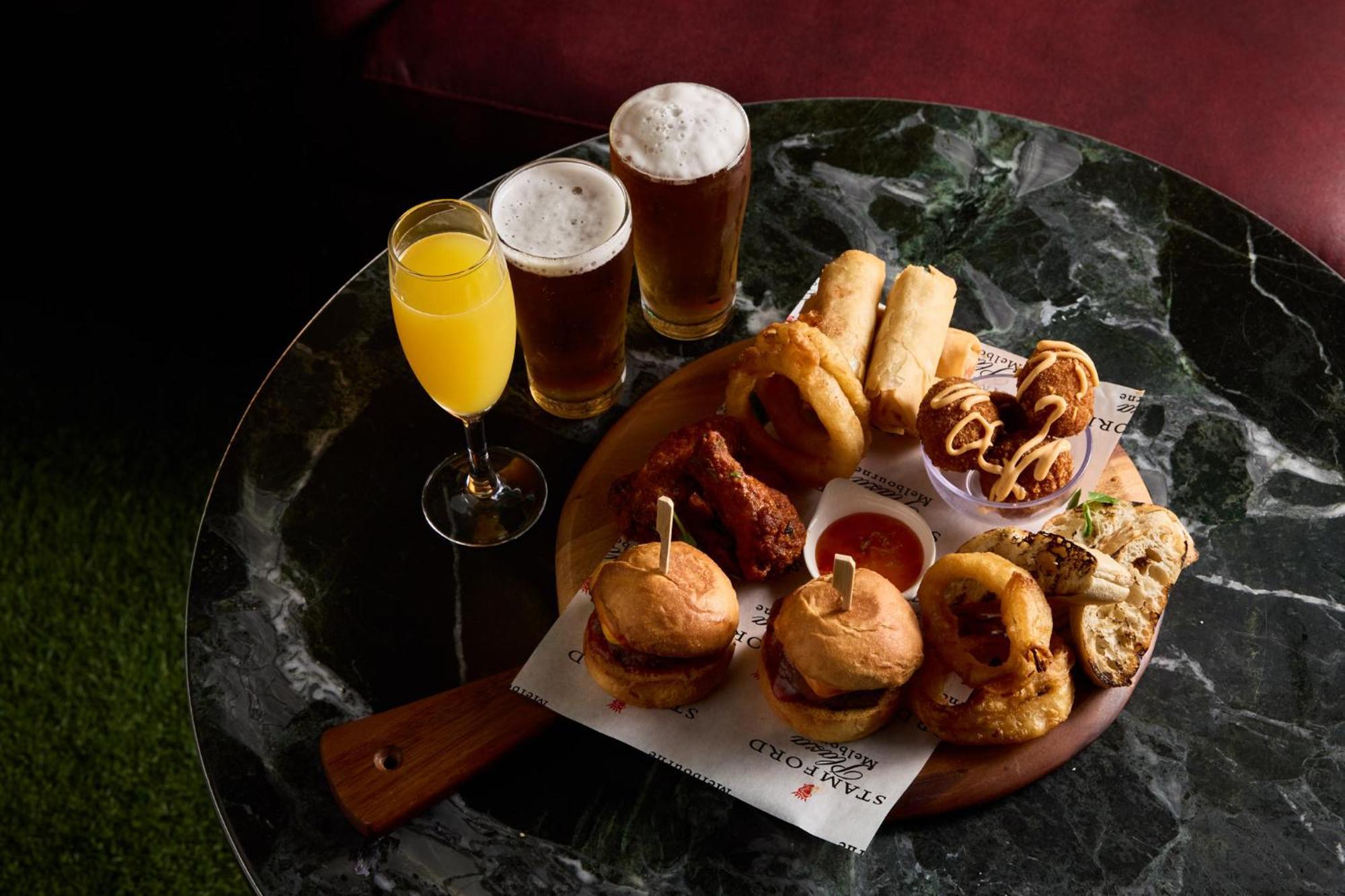 Hotel Stamford Plaza Melbourne Esterno foto The photo displays a variety of food and drinks arranged on a marble table. There are small burgers garnished with skewers, crispy chicken pieces, and deep-fried snacks. Additionally, there are two glasses of beer and a cocktail, likely a mimosa, pre