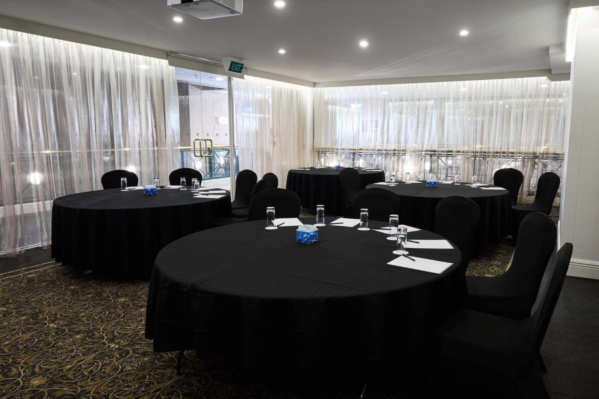 Hotel Stamford Plaza Melbourne Esterno foto The photo shows a meeting or conference room set up with several round tables covered in black tablecloths. Each table is accompanied by black chairs. There are some white notepads and pens placed on the tables, and a small decorative item, possibly 
