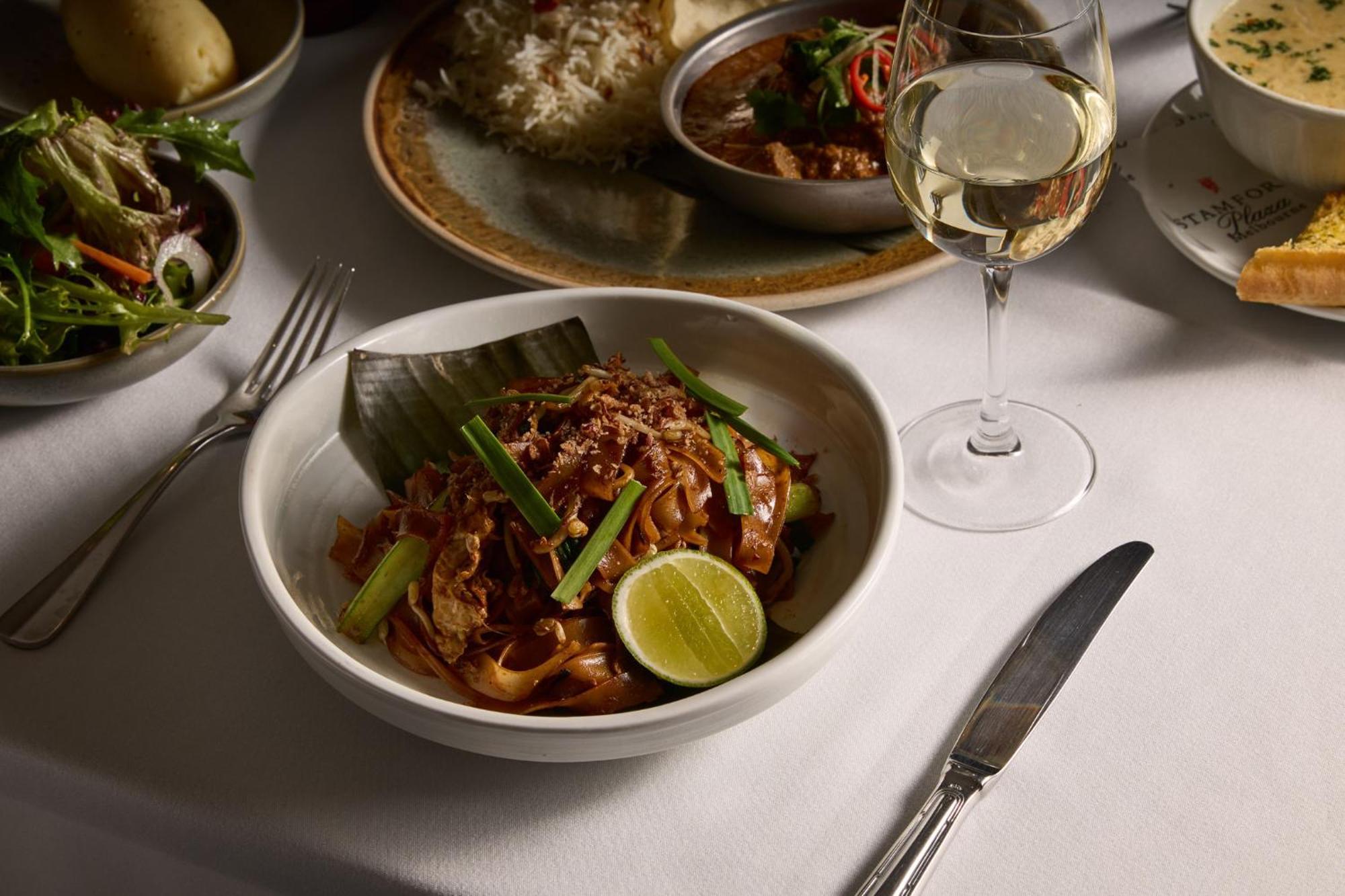 Hotel Stamford Plaza Melbourne Esterno foto The photo features a beautifully arranged dining table with several dishes. In the foreground, there is a bowl of noodles topped with green onions and garnished with a lime wedge. The noodles appear to be stir-fried and have a rich color. Next to the