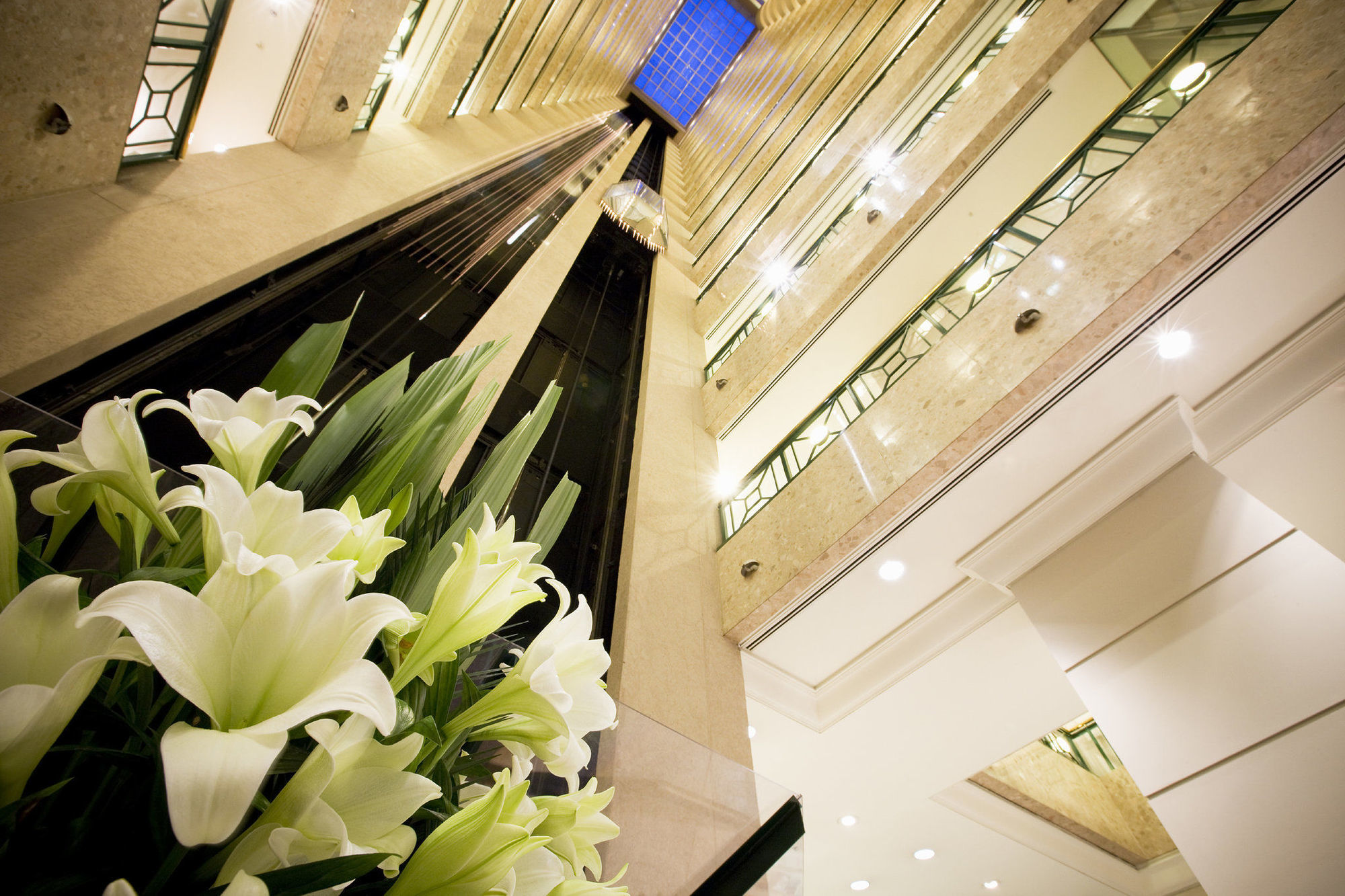 Hotel Stamford Plaza Melbourne Interno foto The photo shows a modern indoor space, likely a lobby or atrium of a building. The view is looking upwards, capturing a sleek design with multiple levels. There are several elevators in the center, running vertically. The walls are lined with glass a